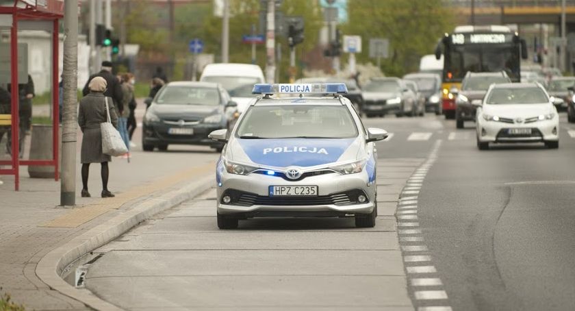 Radiowóz policji obok przystanku autobusowego. W tle inne pojazdy.
